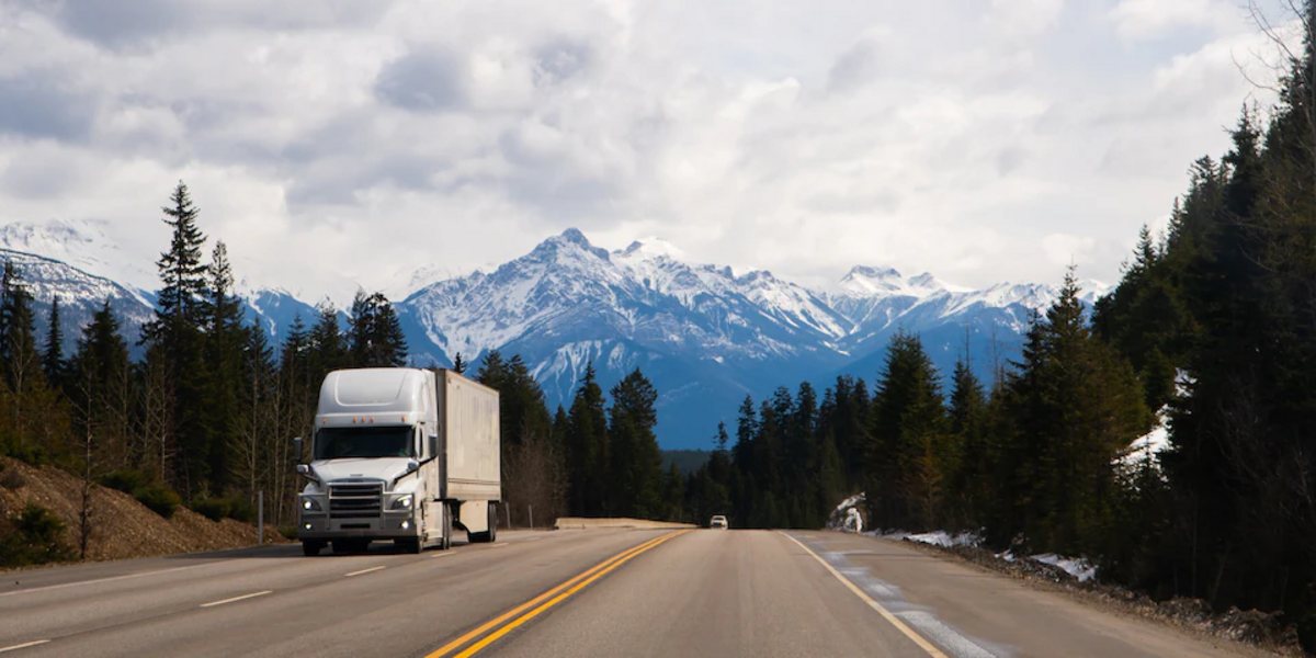 Semi truck on a two lane highway with snowy mountains and pine forest in the Northwest