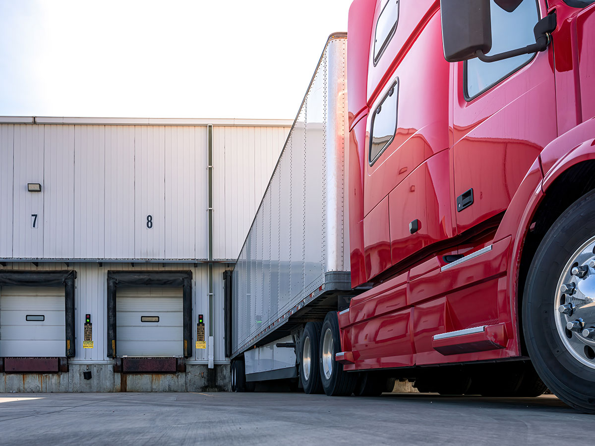 A red semi truck backed up to a warehouse loading dock